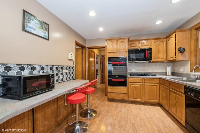 kitchen featuring black appliances, light wood-style flooring, brown cabinets, and a sink