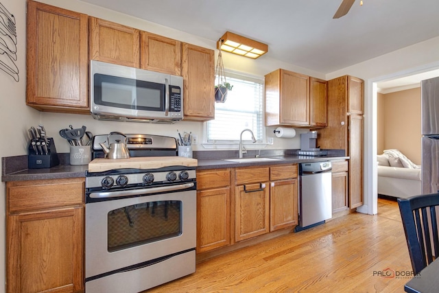 kitchen with stainless steel appliances, dark countertops, a sink, and light wood-style floors