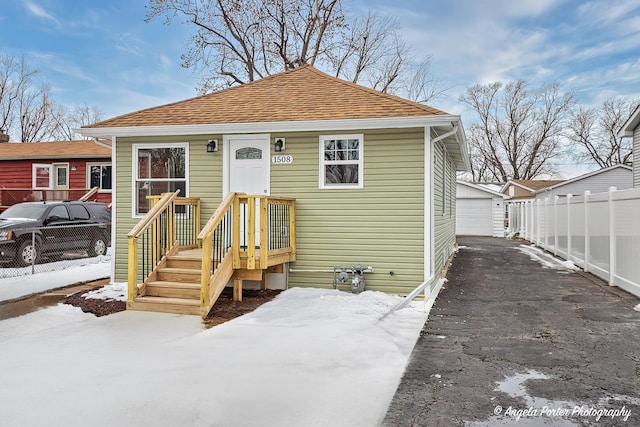 view of front of home featuring a shingled roof, fence, a detached garage, and an outdoor structure