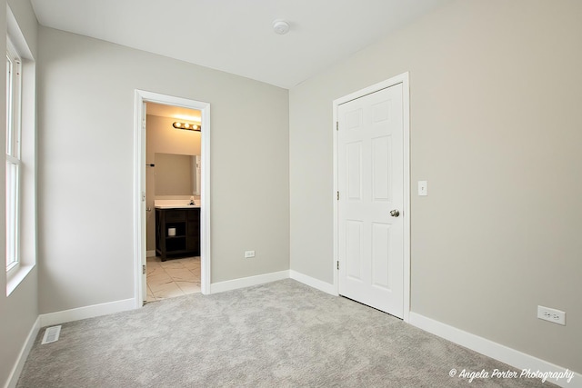 unfurnished bedroom with light carpet, connected bathroom, visible vents, and baseboards