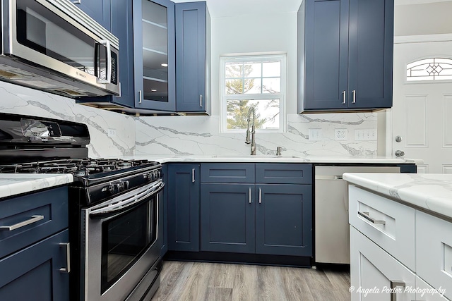 kitchen featuring blue cabinetry, appliances with stainless steel finishes, light wood-style floors, a sink, and light stone countertops