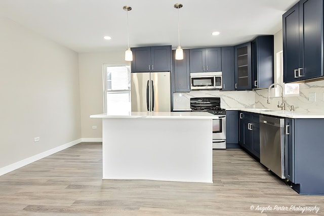 kitchen with light wood finished floors, appliances with stainless steel finishes, a sink, and backsplash