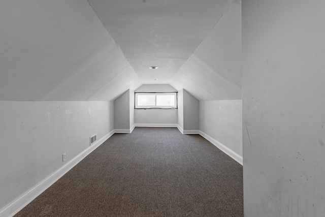 bonus room featuring lofted ceiling, visible vents, dark carpet, and baseboards