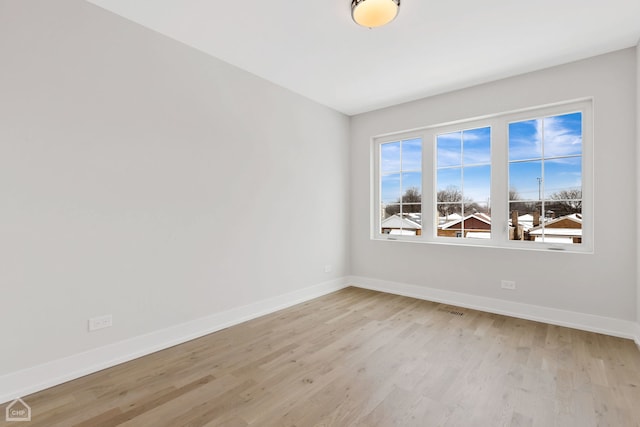 empty room with light wood-type flooring, visible vents, and baseboards