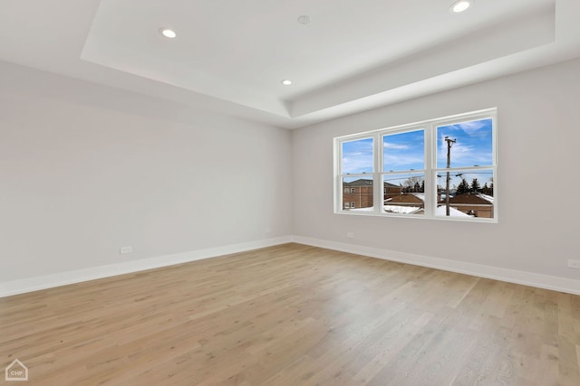 spare room with light wood-type flooring, baseboards, a raised ceiling, and recessed lighting