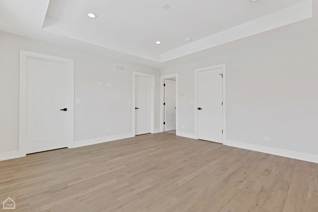 spare room with light wood finished floors, recessed lighting, a raised ceiling, visible vents, and baseboards