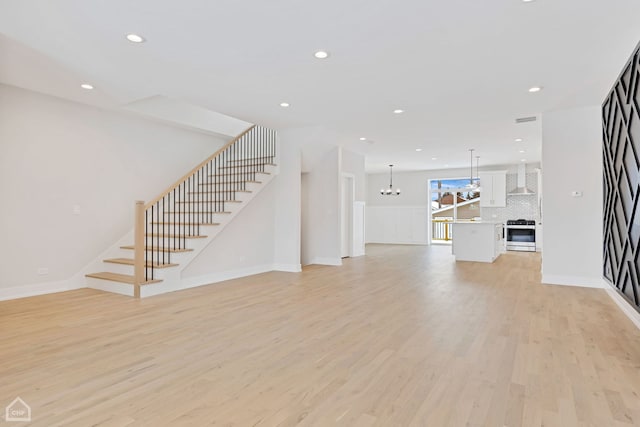 unfurnished living room featuring a chandelier, recessed lighting, light wood finished floors, and stairs