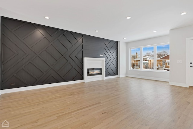 unfurnished living room with recessed lighting, a decorative wall, an accent wall, a glass covered fireplace, and light wood-style floors