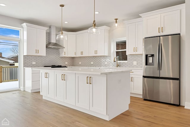 kitchen featuring stainless steel fridge, white cabinets, wall chimney exhaust hood, hanging light fixtures, and light countertops