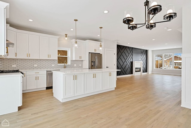 kitchen with open floor plan, stainless steel appliances, a kitchen island, and white cabinetry