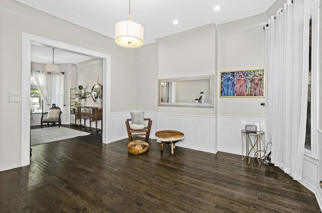 sitting room with a wainscoted wall, a decorative wall, and dark wood-style flooring