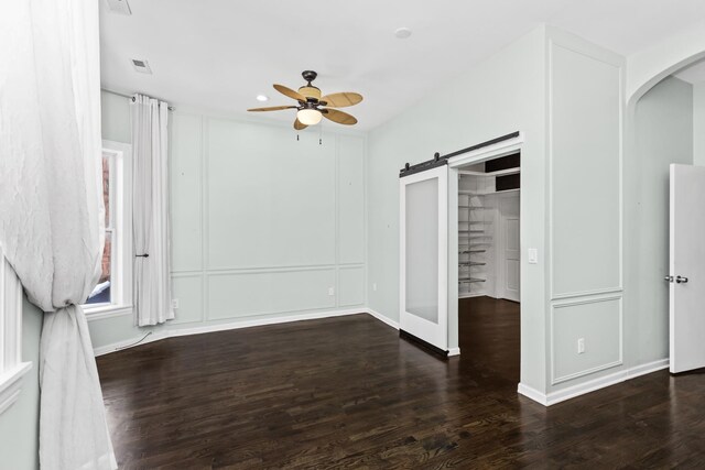 unfurnished bedroom with dark wood finished floors, visible vents, a decorative wall, and a barn door