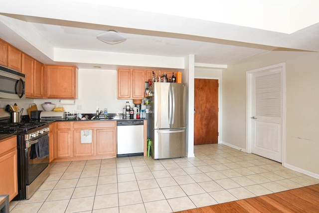 kitchen with light tile patterned flooring, a sink, baseboards, appliances with stainless steel finishes, and dark countertops