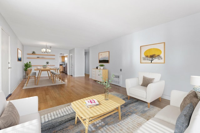 living room featuring heating unit, light wood-style floors, baseboards, and a notable chandelier