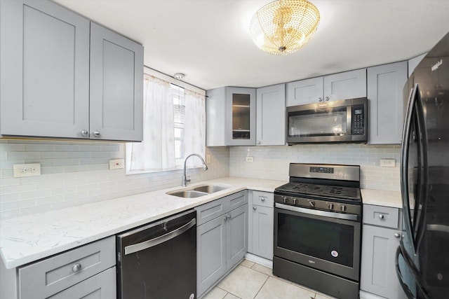 kitchen featuring glass insert cabinets, light stone countertops, gray cabinetry, black appliances, and a sink