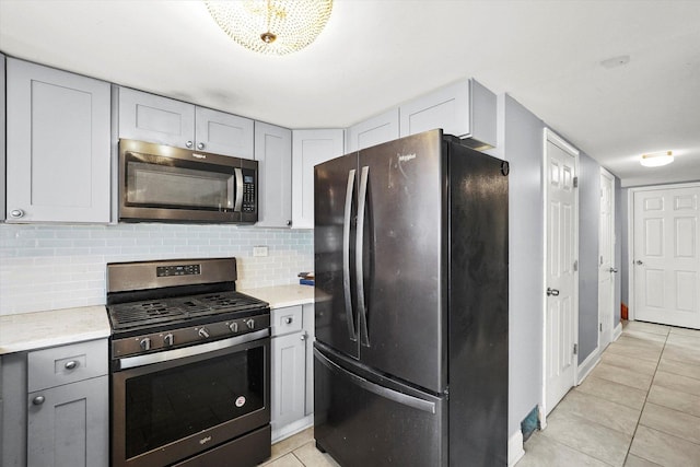 kitchen featuring light tile patterned floors, baseboards, decorative backsplash, stainless steel appliances, and gray cabinetry