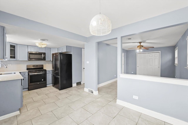 kitchen featuring glass insert cabinets, hanging light fixtures, gray cabinets, stainless steel appliances, and a sink