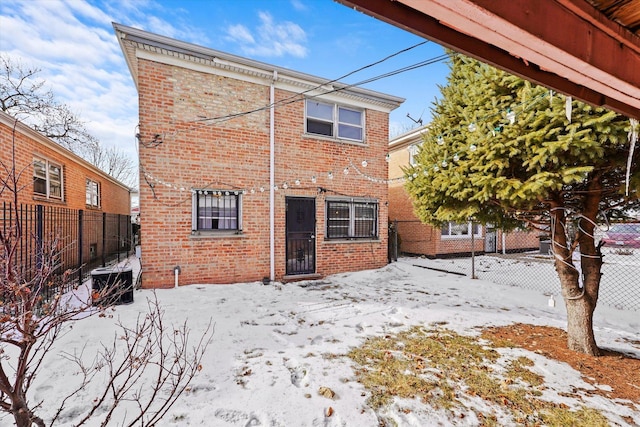 snow covered house with brick siding and fence