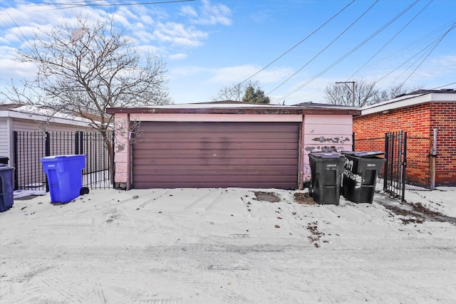 snow covered garage featuring a garage and fence