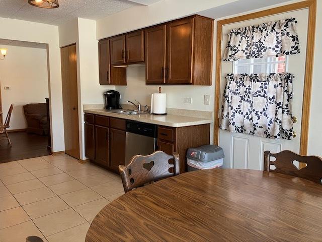 kitchen with light countertops, stainless steel dishwasher, light tile patterned flooring, a sink, and a textured ceiling