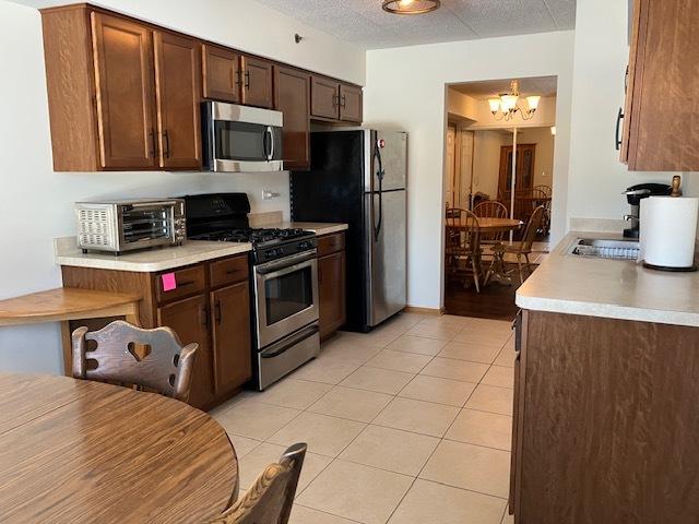 kitchen with a toaster, an inviting chandelier, stainless steel appliances, light countertops, and light tile patterned flooring