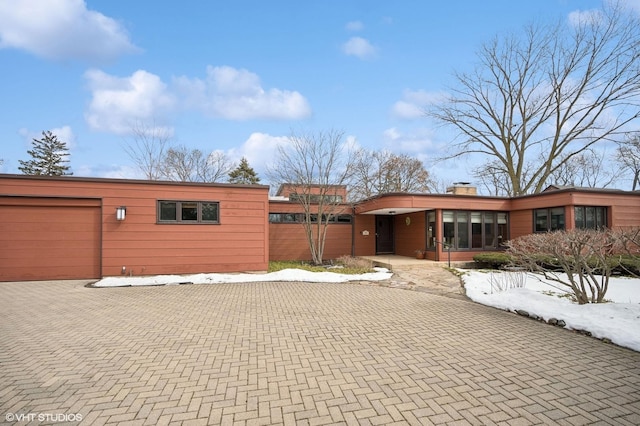 mid-century home featuring an attached garage, a chimney, and decorative driveway