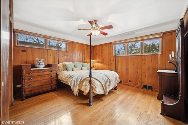 bedroom featuring light wood-type flooring, visible vents, wood walls, and multiple windows