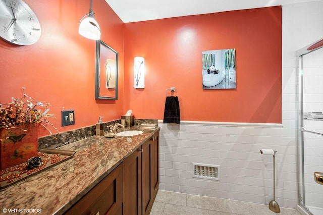 full bath with tile patterned flooring, a wainscoted wall, vanity, visible vents, and tile walls