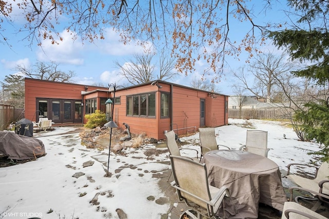 snow covered rear of property with a patio, french doors, and fence