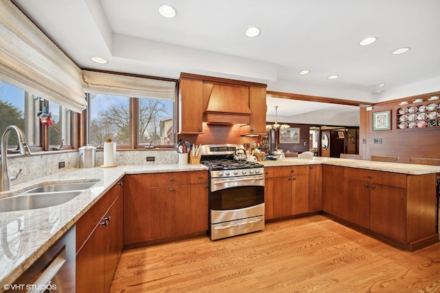 kitchen featuring brown cabinetry, custom range hood, a peninsula, stainless steel appliances, and a sink