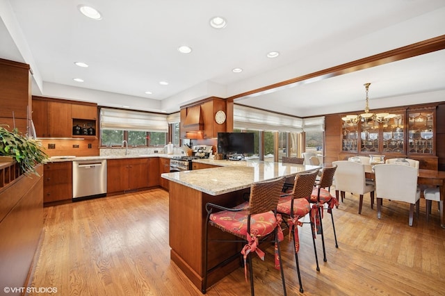 kitchen featuring a chandelier, light stone counters, stainless steel appliances, a peninsula, and brown cabinets