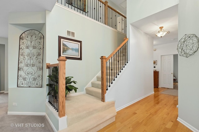 stairway with baseboards, a high ceiling, visible vents, and wood finished floors