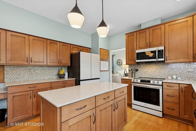 kitchen with decorative light fixtures, light wood finished floors, decorative backsplash, appliances with stainless steel finishes, and a kitchen island