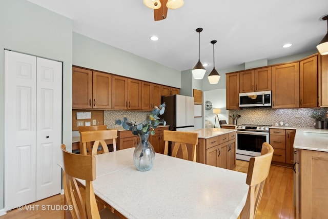 kitchen featuring brown cabinets, pendant lighting, stainless steel appliances, and light countertops