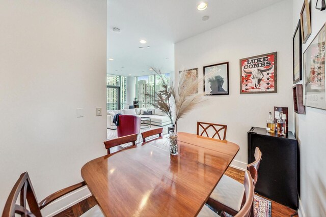 dining area featuring baseboards, a wall of windows, wood finished floors, and recessed lighting