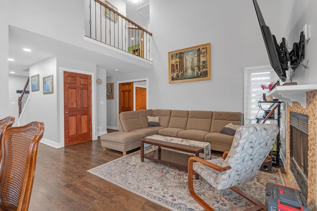 living area featuring a fireplace, stairway, a high ceiling, dark wood-type flooring, and baseboards