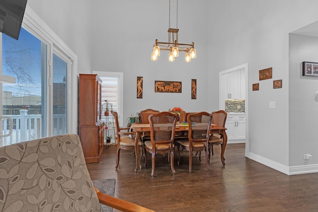 dining space featuring a notable chandelier, a high ceiling, dark wood finished floors, and baseboards