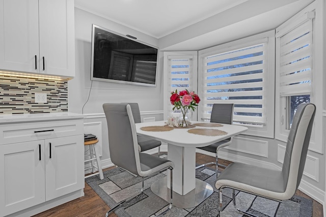 dining space featuring crown molding, dark wood finished floors, and a decorative wall