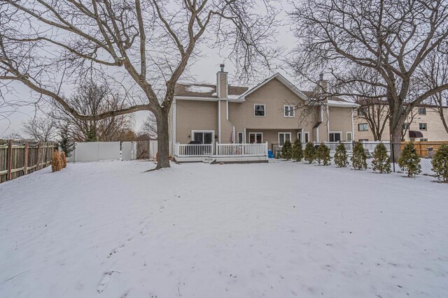 snow covered back of property featuring a chimney and fence private yard