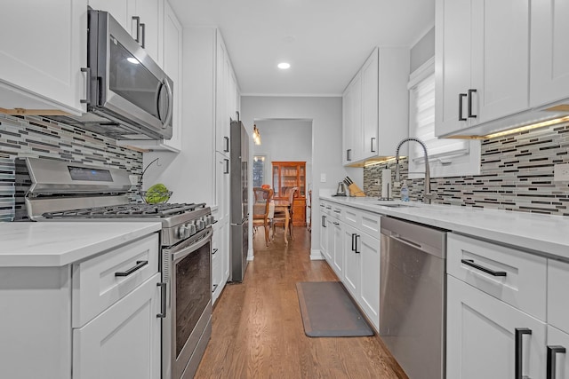 kitchen with light stone counters, light wood-style flooring, a sink, white cabinets, and appliances with stainless steel finishes