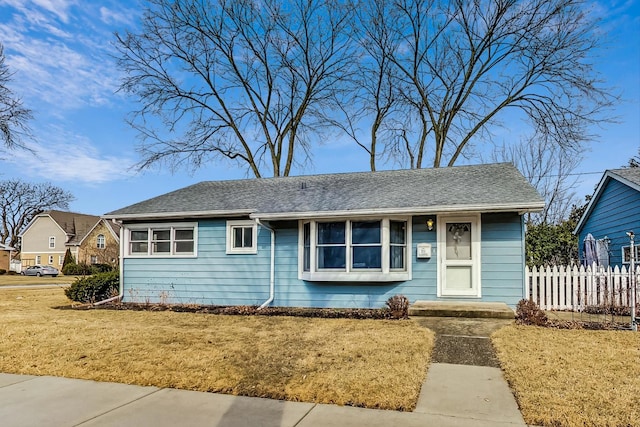 view of front of house with fence, a front lawn, and roof with shingles