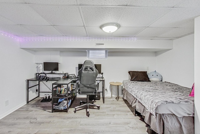 bedroom with a drop ceiling, visible vents, baseboards, and wood finished floors