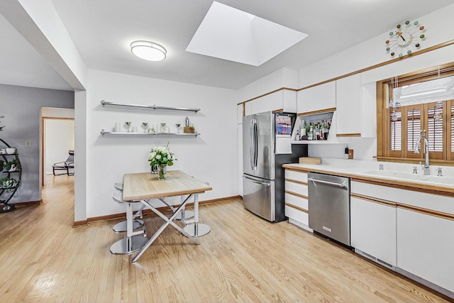 kitchen with a skylight, stainless steel appliances, light wood-style floors, white cabinetry, and a sink