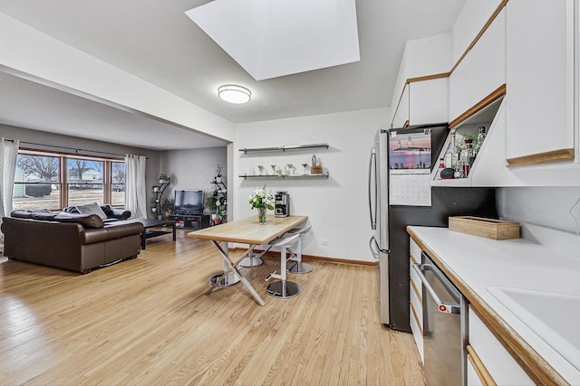 kitchen featuring a sink, white cabinetry, light countertops, stainless steel dishwasher, and light wood finished floors