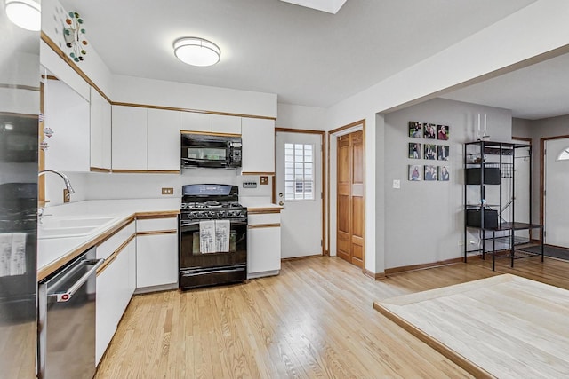 kitchen featuring light countertops, light wood-style flooring, white cabinets, a sink, and black appliances