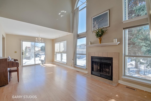 living area with a notable chandelier, visible vents, light wood-style flooring, a high ceiling, and a tiled fireplace