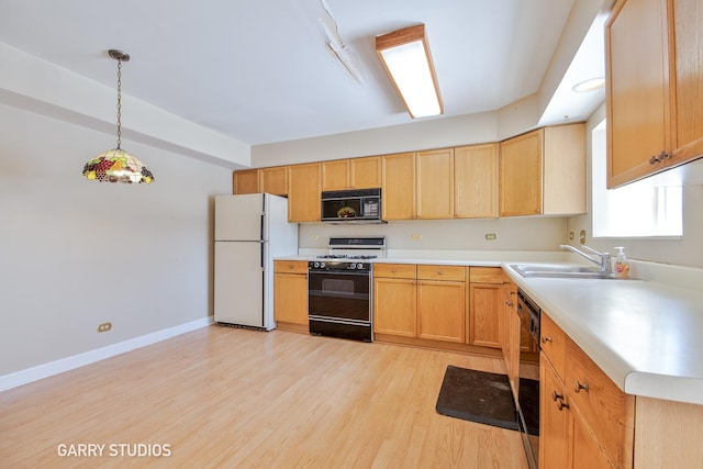 kitchen with light wood finished floors, light countertops, black appliances, pendant lighting, and a sink