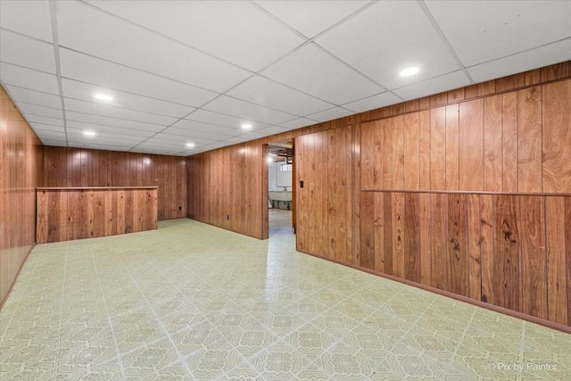 finished basement with wooden walls, tile patterned floors, and a paneled ceiling