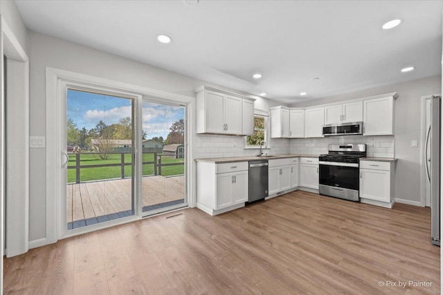 kitchen with decorative backsplash, stainless steel appliances, light wood-style flooring, and white cabinets