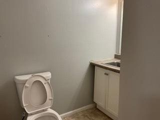 half bathroom featuring toilet, vanity, and baseboards